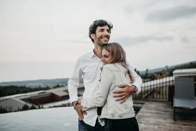 A couple embracing on a rooftop terrace, with hills and a cloudy sky behind them, representing the relationship effects of porn addiction.